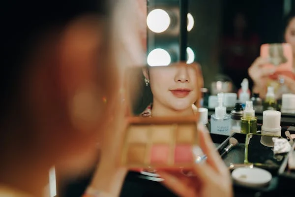 woman at a makeup desk looking into a small mirror