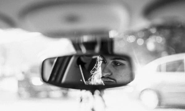 Man' reflection in the rear vision mirror of a car